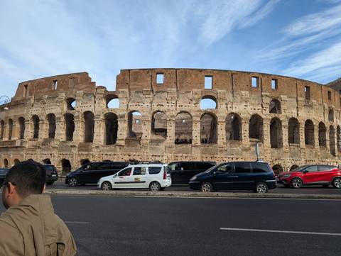       Large ancient amphitheater with vehicles parked outside.
  