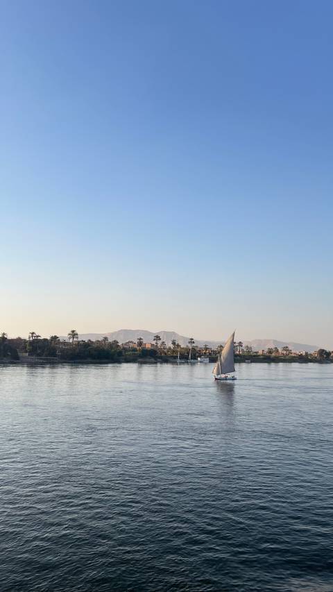 Tranquil river scene with a sailboat and distant mountains.