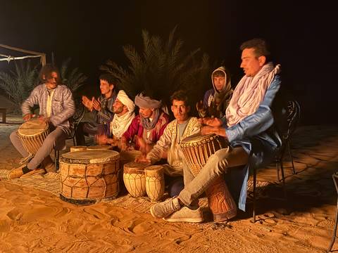 Group of people sitting on the sand playing traditional drums at night.