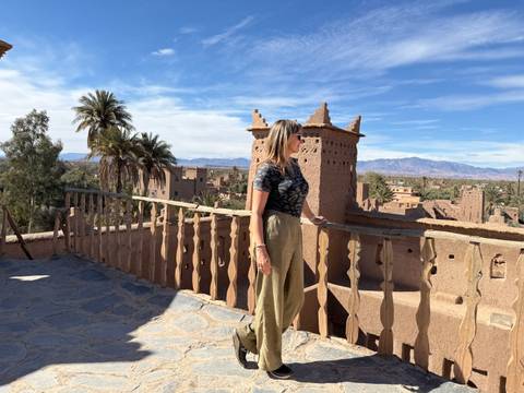 A woman standing on a rooftop with a view of traditional Moroccan architecture and palm trees.
