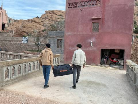 Two men carrying a bag walking past a traditional Moroccan building.