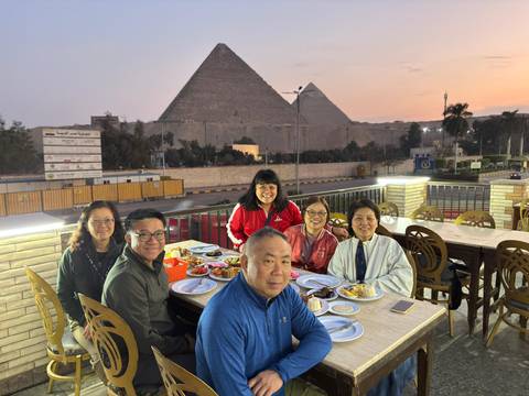 Group of people dining outdoors with the pyramids in the background during sunset.