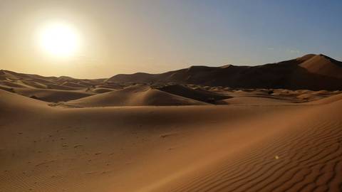 Rolling sand dunes with clear sky and setting sun.