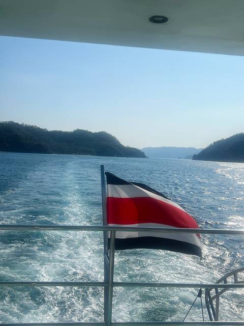       Boat cruising away leaving a trail with a national flag visible.
  