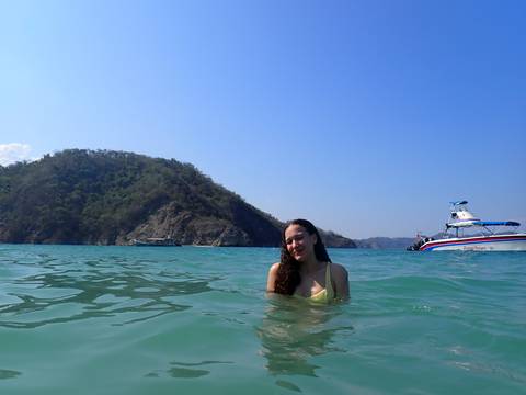       Woman in the sea near a boat with a scenic background.
  