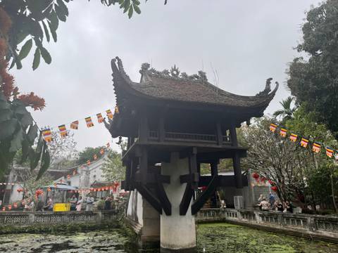       A pagoda in an outdoor temple area surrounded by flags and visitors.
  