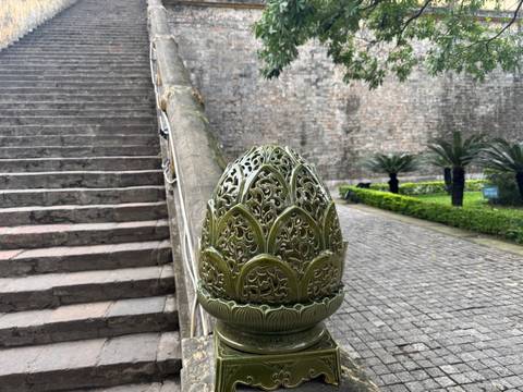       Detailed view of an ornate railing with stone steps and garden.
  