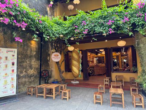      Charming cafe facade with flowering vines and seating.
  