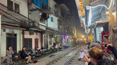       A bustling narrow street with cafes alongside a train track.
  