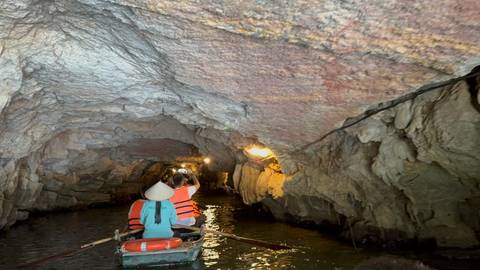       Tourists on a boat inside a dimly lit cave.
  