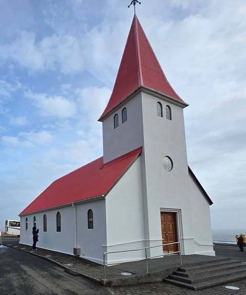 Small church with a red roof and white walls against a cloudy sky.