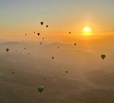 Hot air balloons floating over a desert landscape at sunrise.