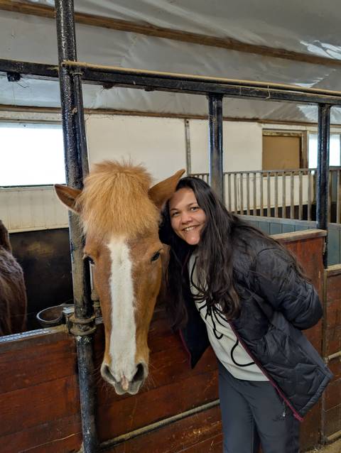       Person smiling with an Icelandic horse in a stable.
  