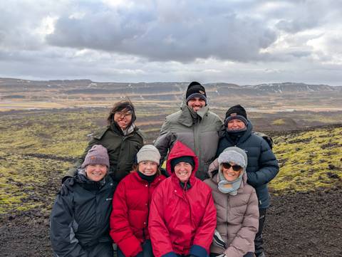       Group of people in warm clothing on a hilltop with vast scenery.
  