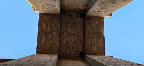 View upwards towards a ceiling with hieroglyphics and clear blue sky around.