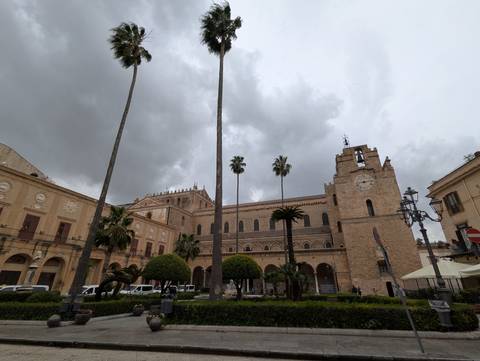       Historic building with clock tower and palm trees under a cloudy sky.
  