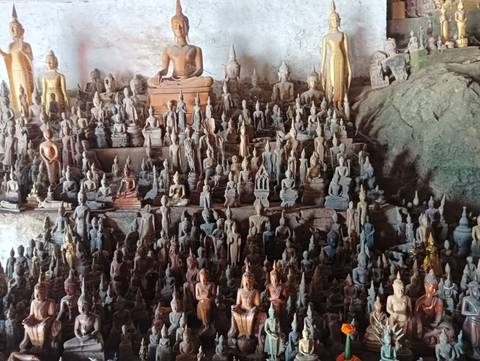 Numerous small Buddha statues on display in a rock cave.