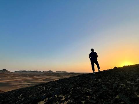       Silhouette of a person standing on a rocky hill during sunset.
  