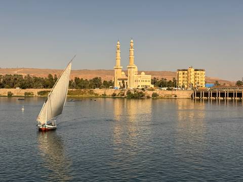 A traditional boat sailing on a river with a mosque in the background.