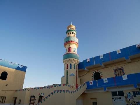       A colorful mosque with a tall minaret against a clear sky.
  