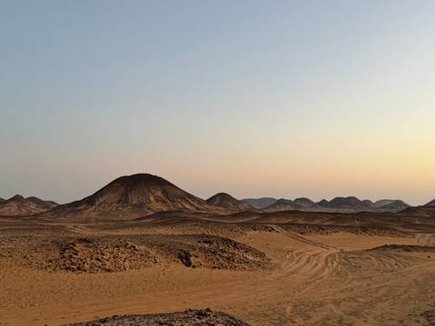       A serene desert landscape with small hills at sunset.
  