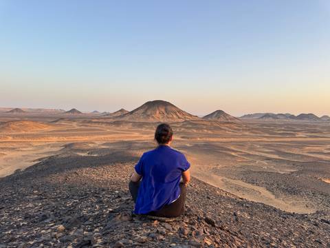       Person sitting on a hill overlooking a barren landscape.
  