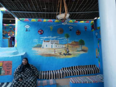 A woman sitting by a decorative mural in an Egyptian house.