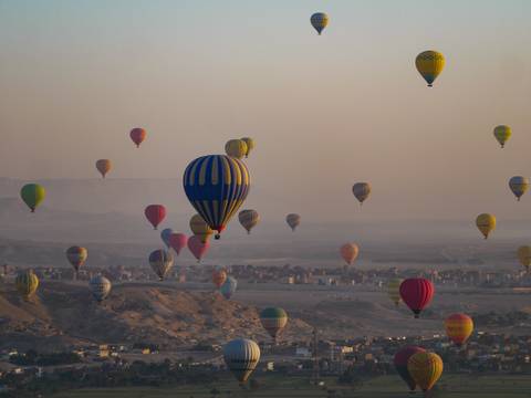       Hot air balloons floating over an Egyptian desert landscape.
  