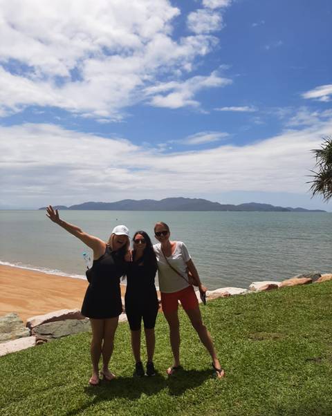 Three people posing by the beach with an ocean and mountains in the background.