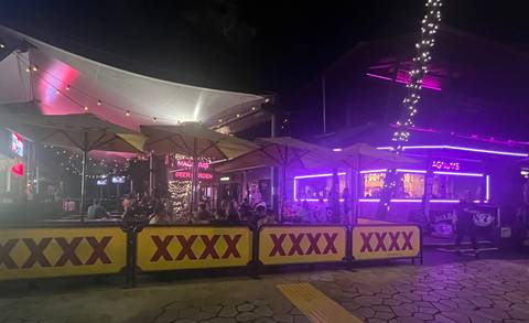 Outdoor bar with neon lights and customers at night.