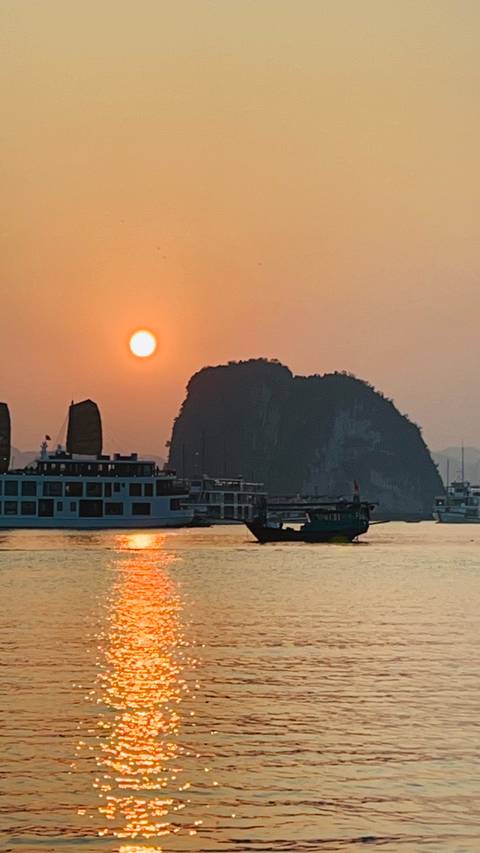 Boats on the sea with the sun setting behind cliffs.