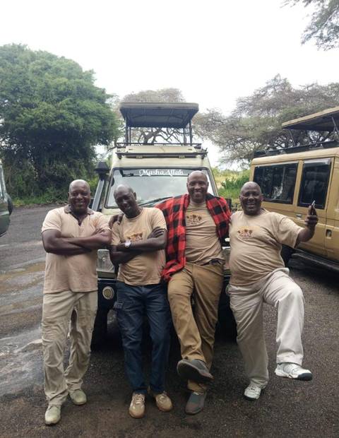       Four people posing in front of safari vehicles.
  