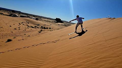       Person sandboarding down a desert dune.
  