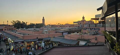       Busy market square at sunset with minaret and buildings.
  