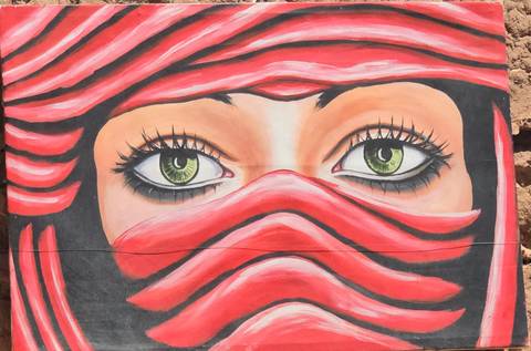       Close-up of a colorful mural with green eyes and a red headscarf.
  