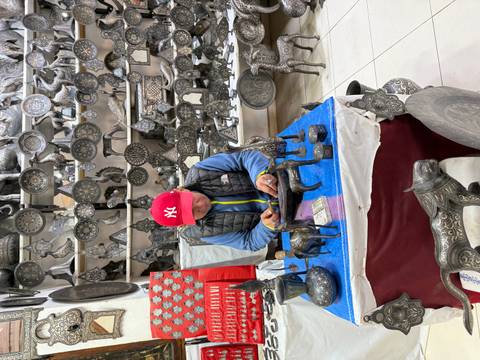 Artisan working on metal crafts surrounded by decorative items.