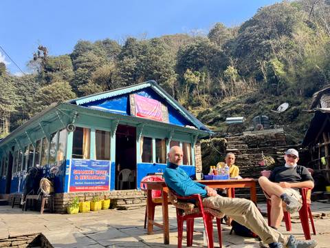 People sitting outside a small cafe with mountains behind.