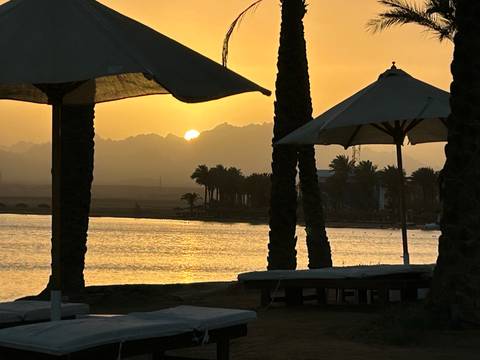 Beach scene with sun umbrellas and distant mountains at sunset.