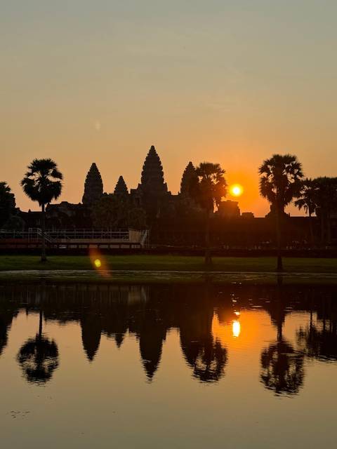 Silhouetted Angkor Wat temple complex with sunset in the background.