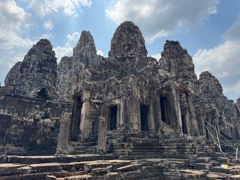 Ancient temple ruins with intricate stone carvings under a partly cloudy sky.