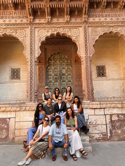 Group of women sitting on steps in front of an ornately carved door.