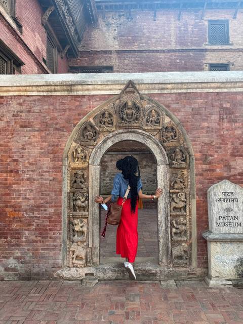 Person standing in front of an intricately carved doorway at Patan Museum.
