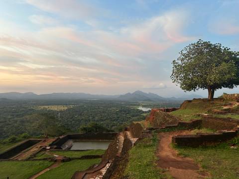 Mountainous landscape with a solitary tree and ruins at sunset.