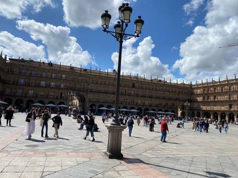       Large city square bustling with people under a partly cloudy sky.
  