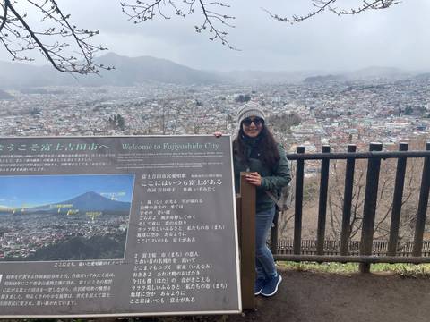       Woman standing beside a city sign with a panoramic view in the background.
  