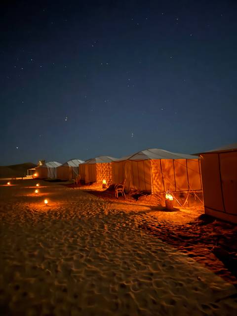       Desert camp illuminated at night with tents.
  
