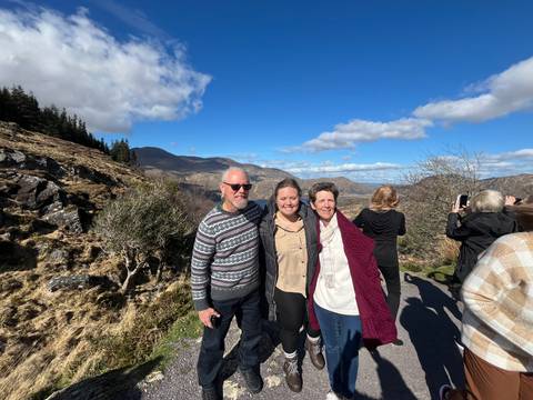 Three people posing with a mountainous landscape in the background.