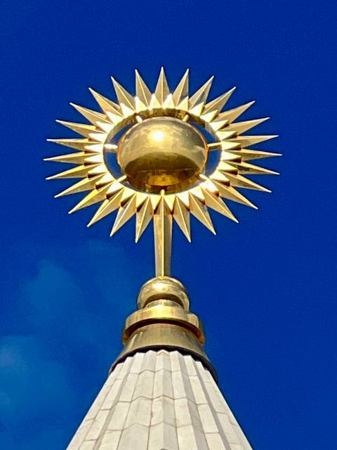       Golden sun sculpture on a spire.
  