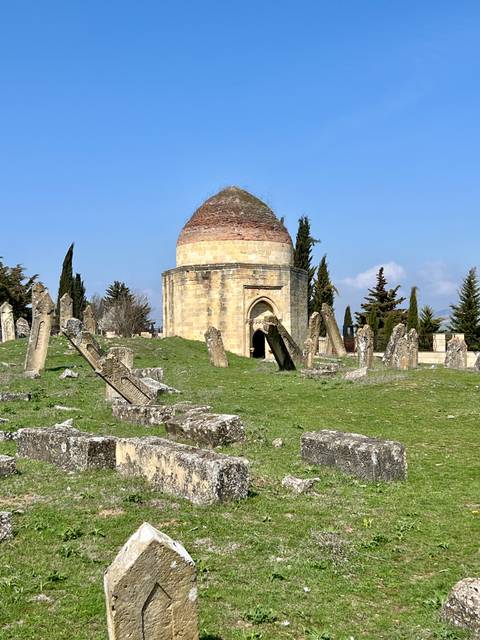       Historic site with stone structures and tombstones under a blue sky.
  