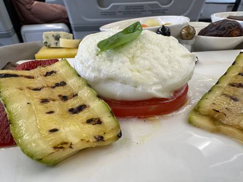       Plate with various grilled vegetables and cheese beside a glass of water.
  